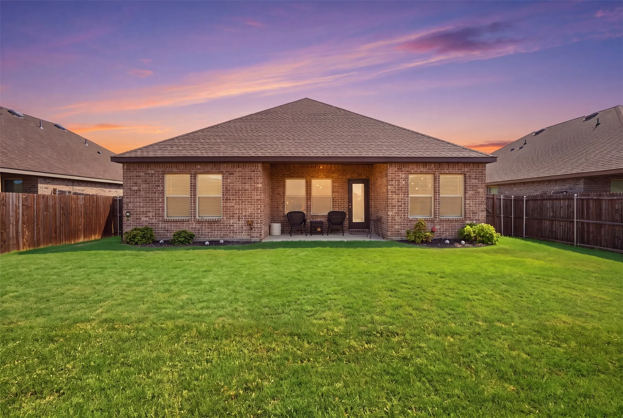 Expansive backyard featuring a manicured lawn, brick exterior, covered patio, and privacy fencing