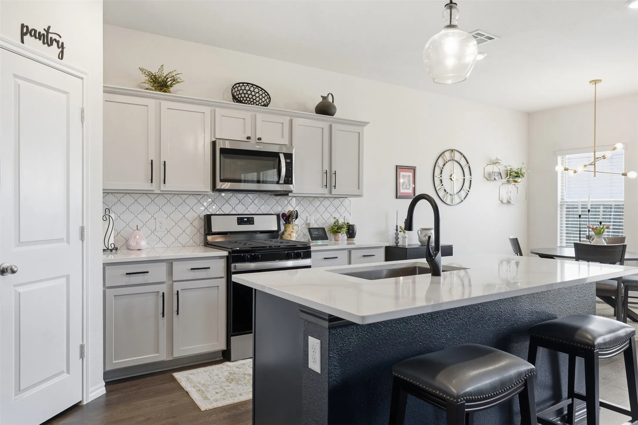 Kitchen featuring light grey cabinetry, stainless steel appliances, a tile backsplash, a dark-toned island with a white countertop, and wood-finish flooring