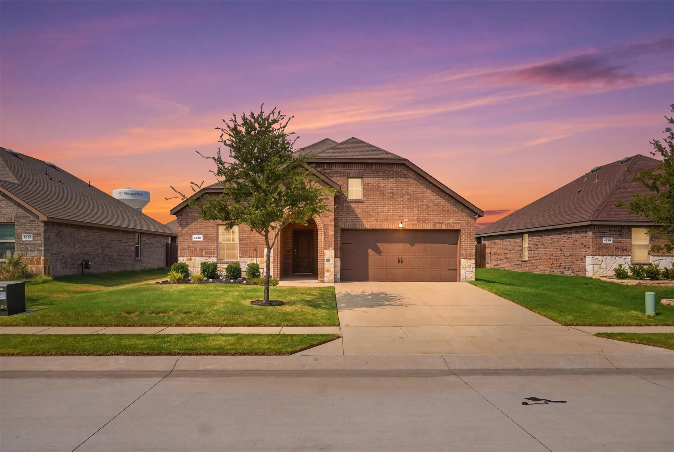 Brick exterior with a stone accent facade, attached garage, concrete driveway, and a front yard with mature landscaping