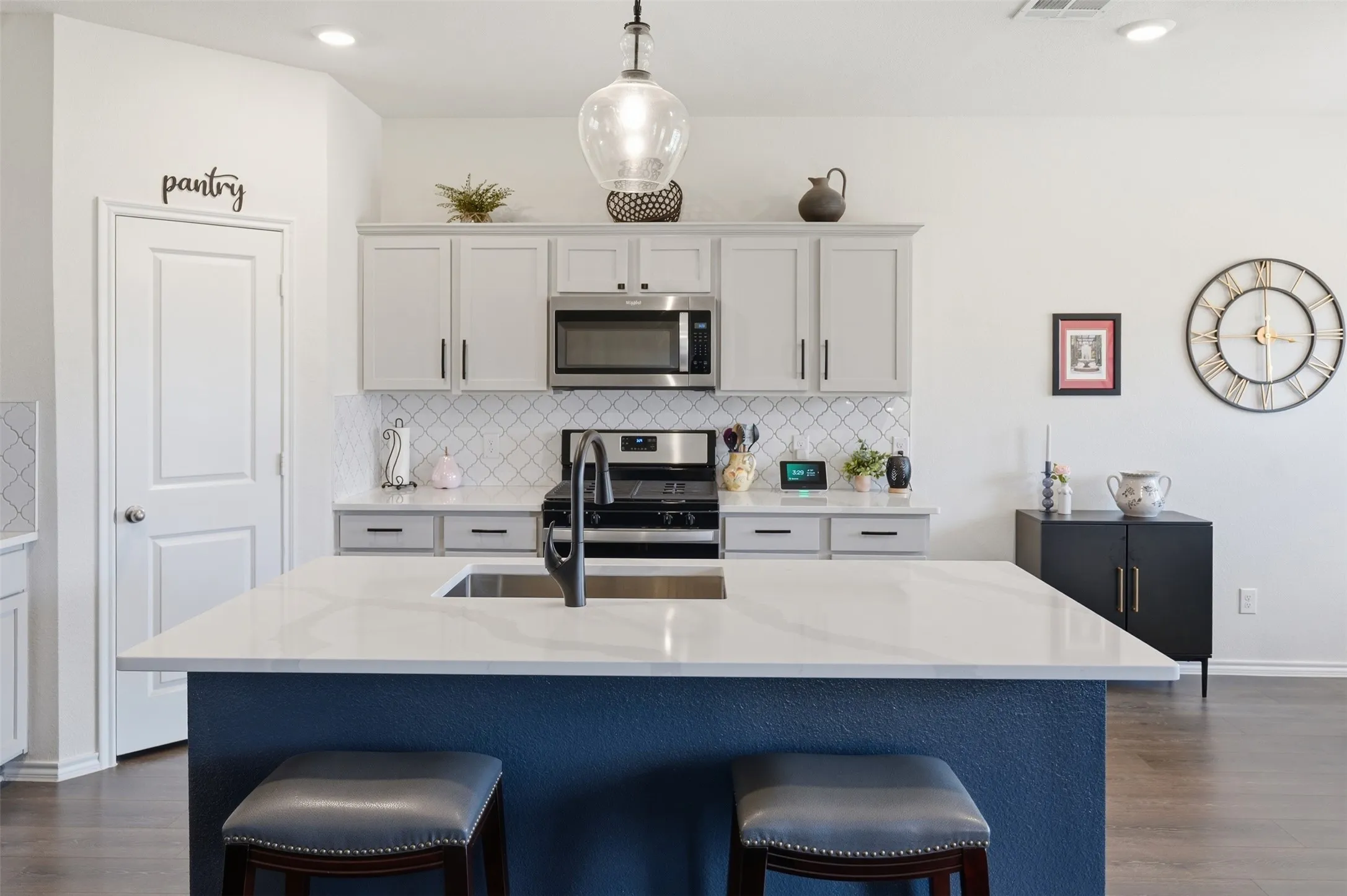Kitchen island with a white countertop and integrated sink, stainless steel microwave, light-toned cabinetry, subway tile backsplash, and wood-finish flooring