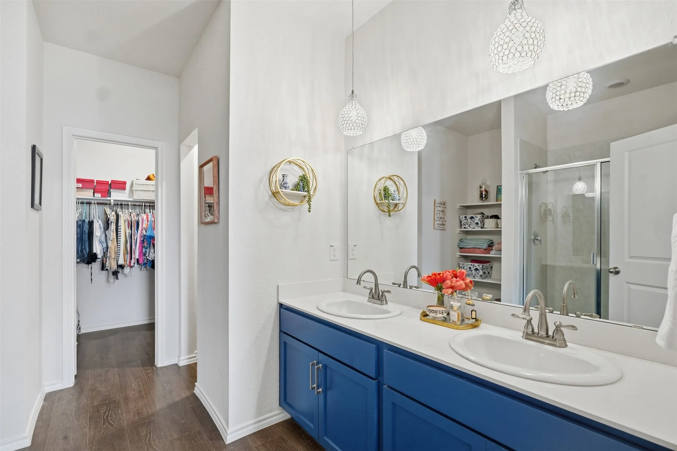 Dual basin vanity with blue cabinetry, expansive wall-mounted mirror, and wood-finish flooring