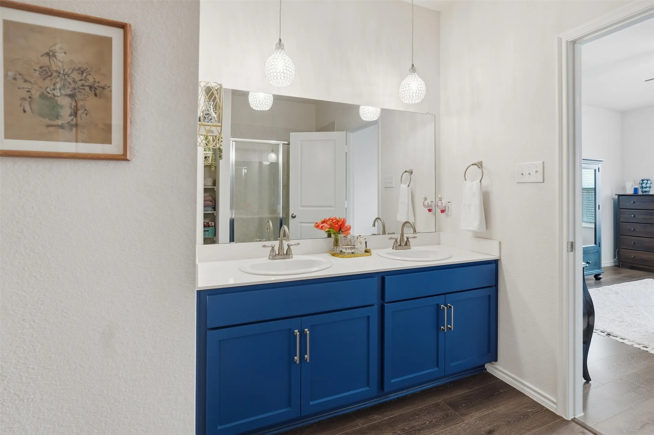 Dual vanity with white countertop and integrated sinks, blue cabinetry with brushed nickel hardware, two pendant light fixtures, and wood-finish flooring