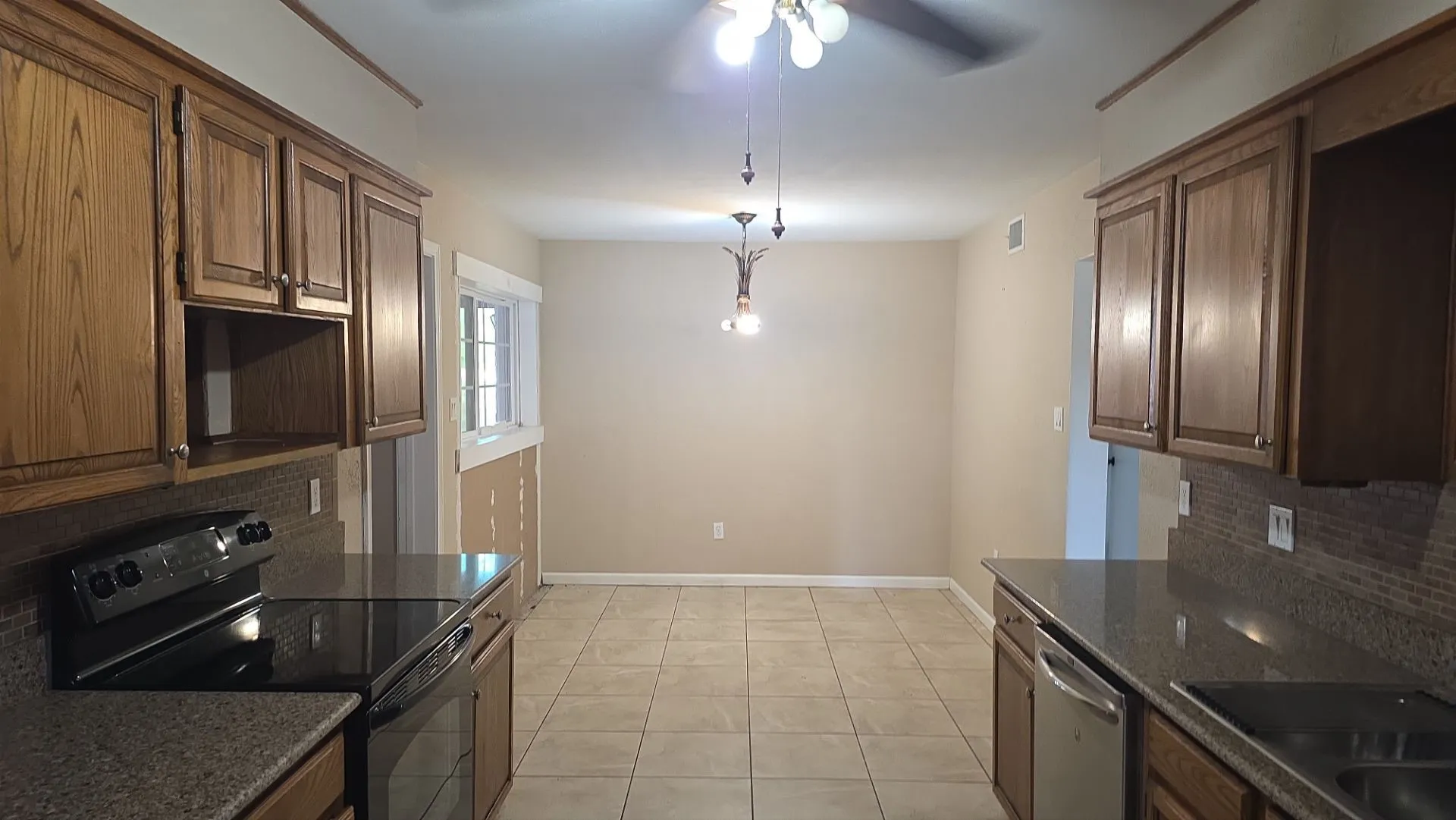 Kitchen featuring wood-finish cabinetry, dark granite countertops, and a full tile backsplash