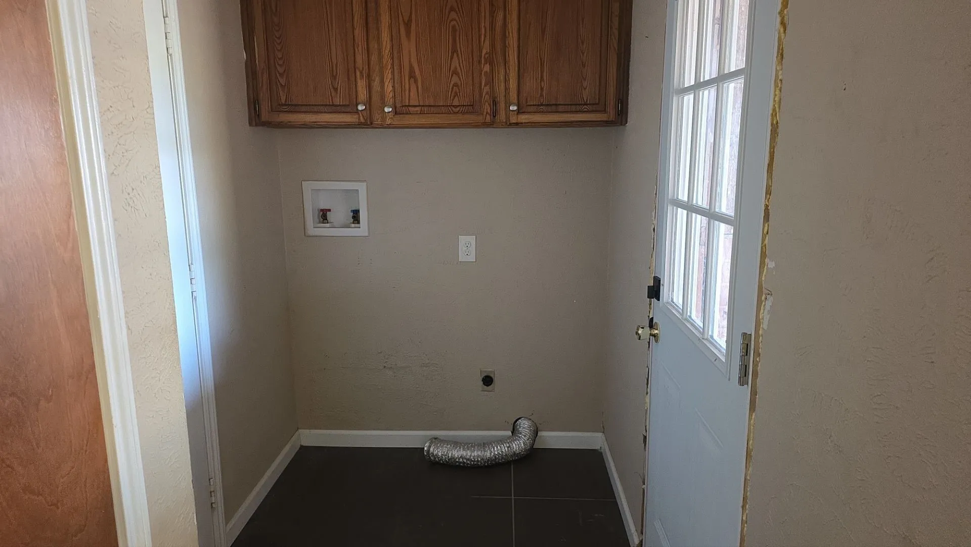 Laundry area with wood-finish cabinetry, dark tile flooring, and a glass-paneled exterior door