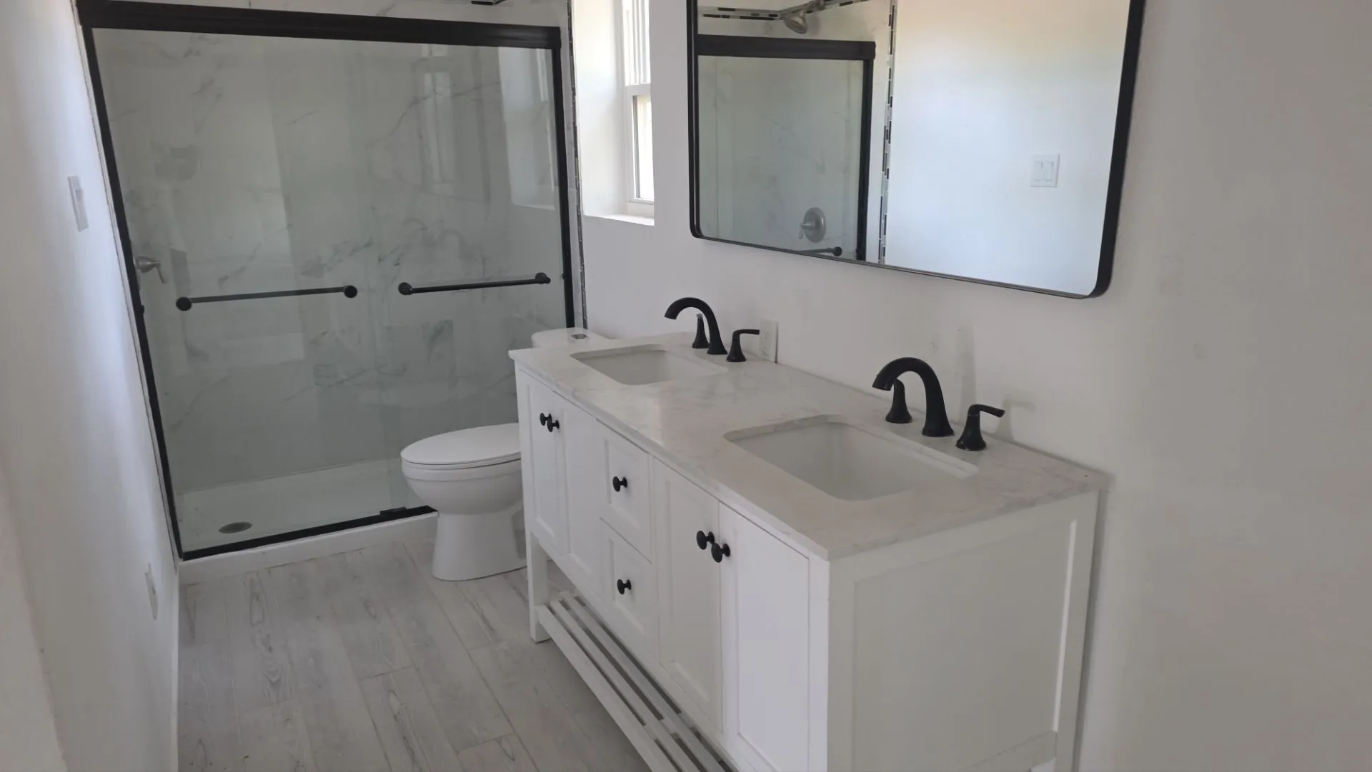 Dual vanity with integrated sinks and matte black fixtures, framed mirror, and a glass-enclosed shower with a black frame