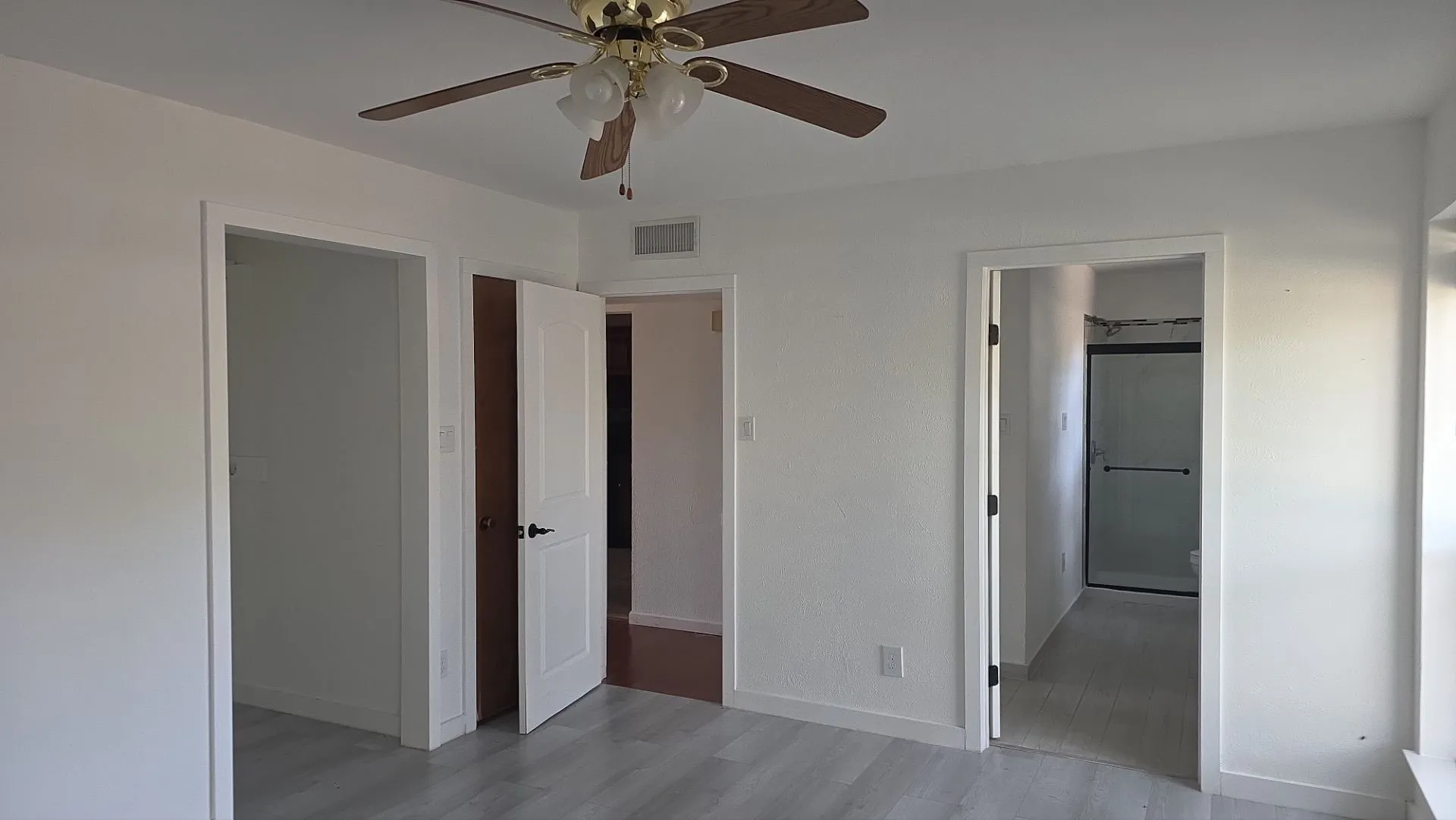 Light wood-finish flooring, ceiling fan with light fixture, white interior doors, and a shower enclosure