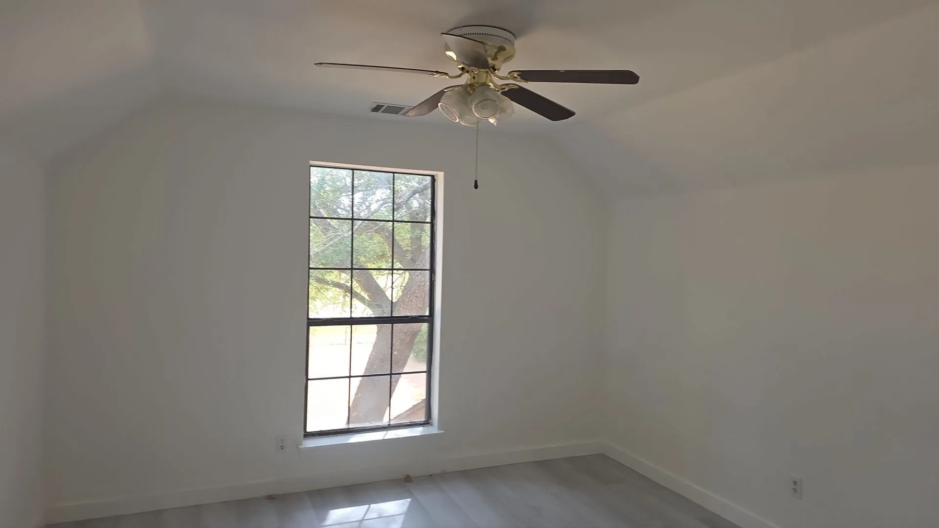 Vaulted ceiling with a ceiling fan, a large window with grid pattern, and wood-finish flooring