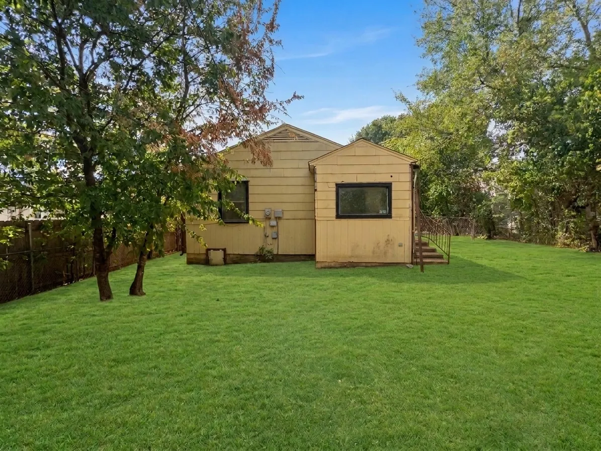 Expansive lawn area with a chain-link fence border and mature trees