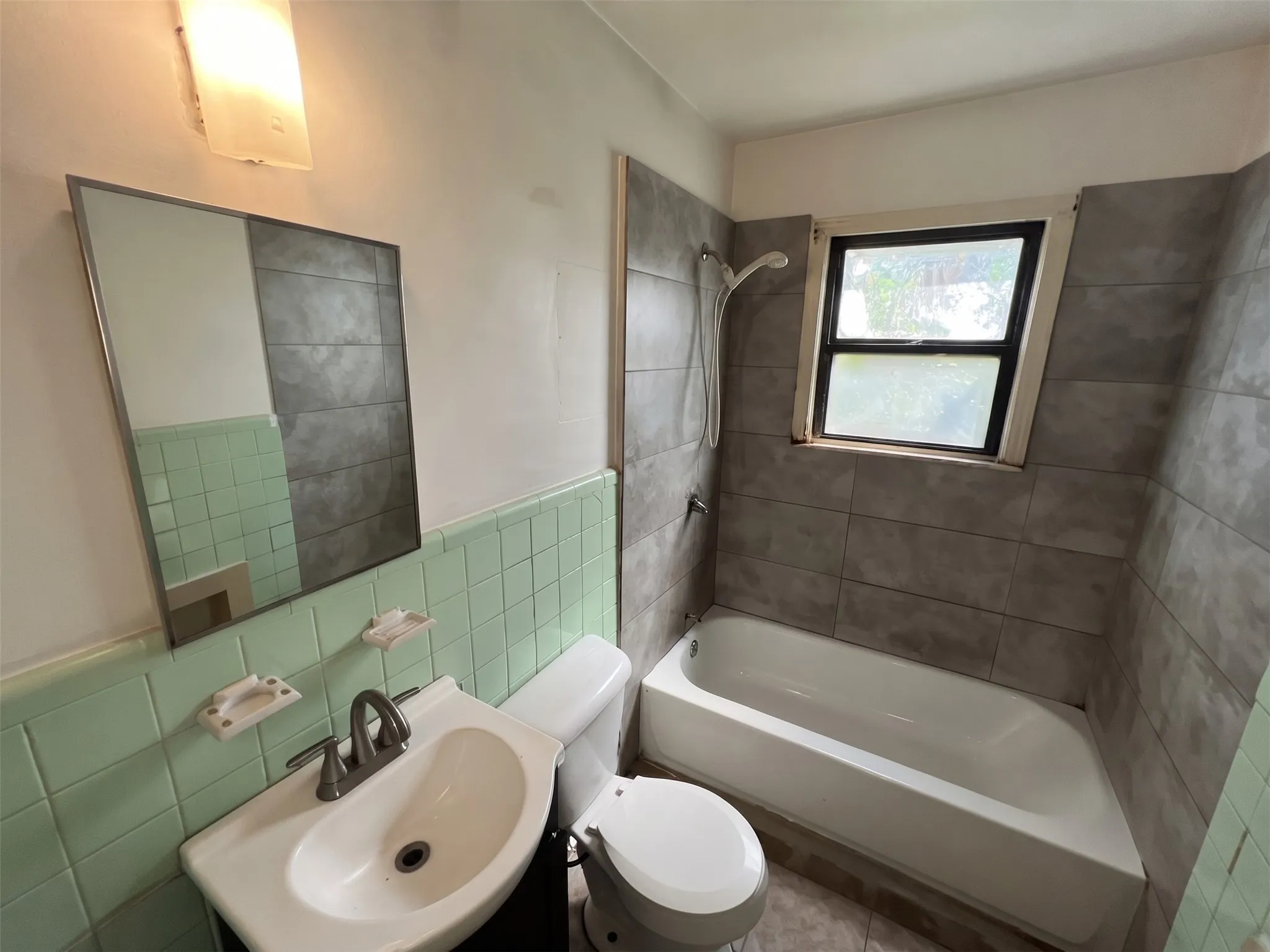 Full bathroom featuring a white porcelain tub, a white vanity with an integrated sink, a wall-mounted mirror, and a window