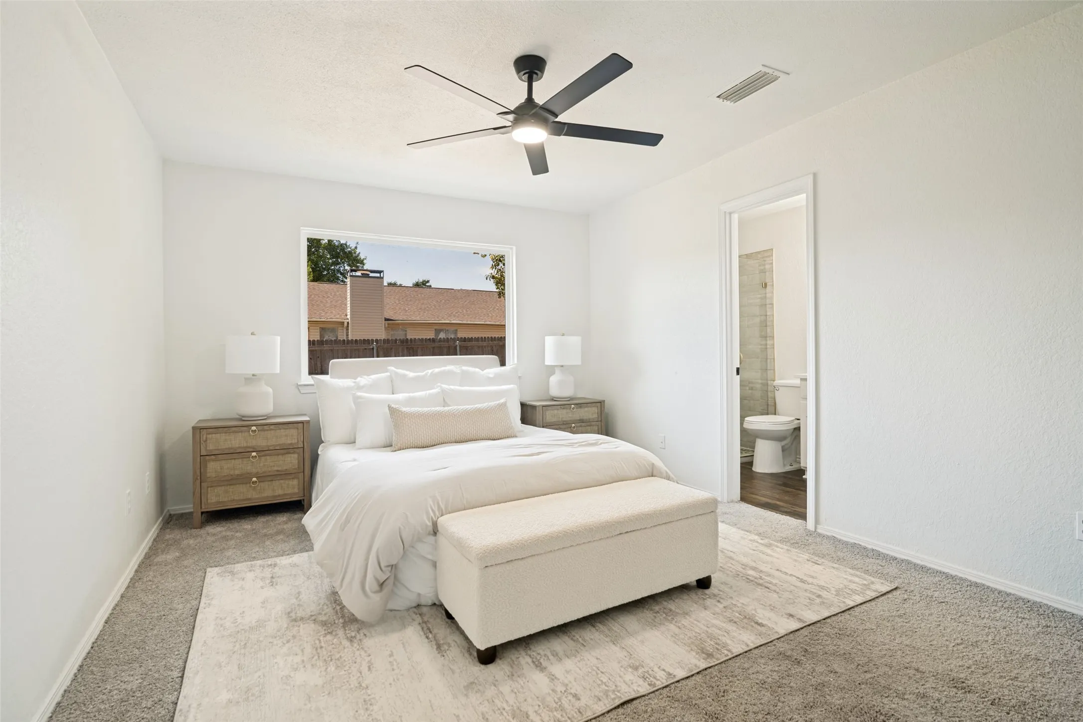 Carpeted room featuring a ceiling fan, a window, and an open doorway revealing a bathroom with wood-finish flooring and a toilet