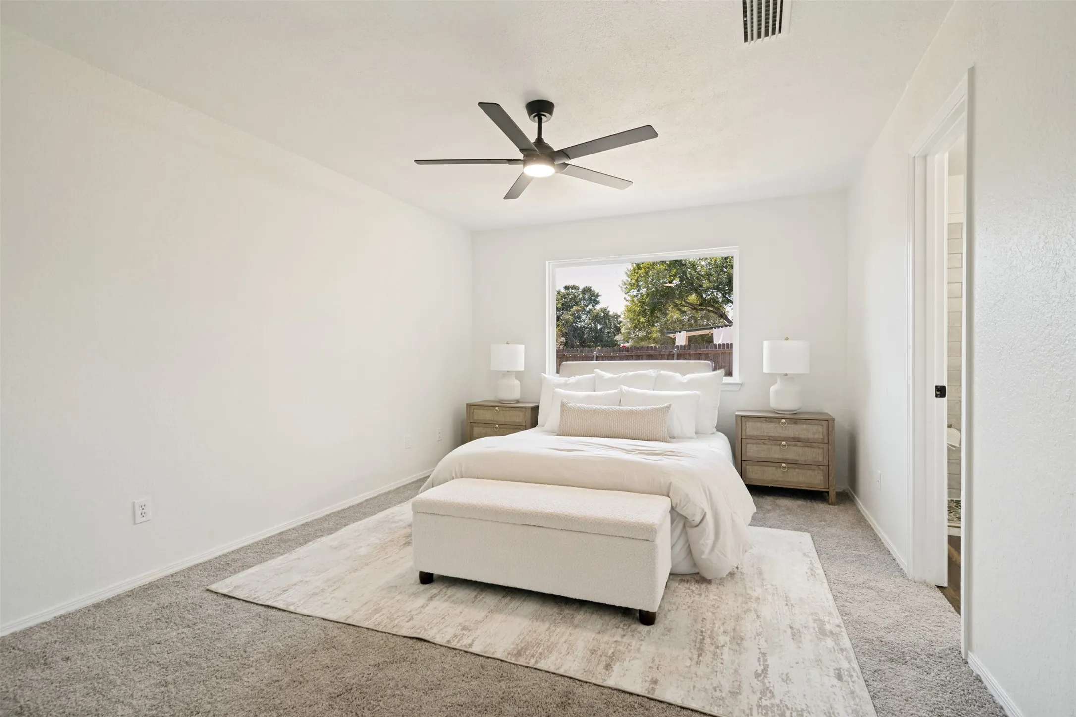 White walls and ceiling, gray textured carpeting, and a ceiling fan with integrated lighting
