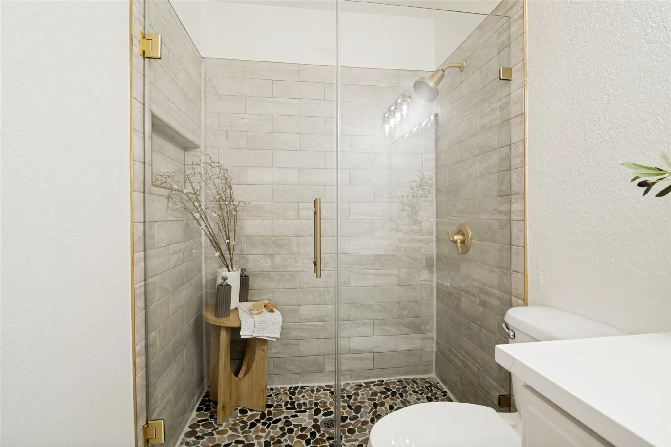 Glass-enclosed shower with gold-tone hardware, horizontal subway tile, and a river rock shower floor
