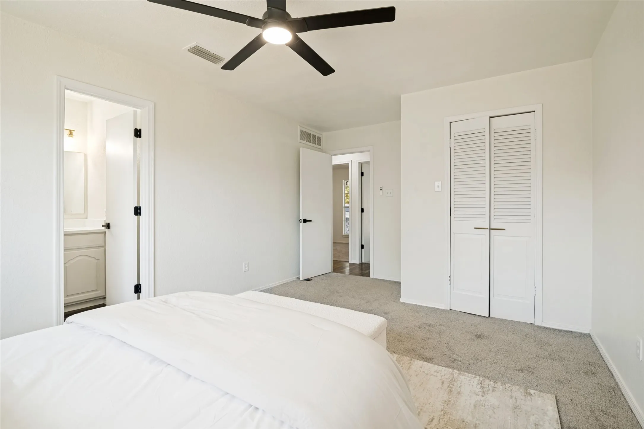 Carpeted room featuring a ceiling fan, louvered closet doors, and an en-suite bathroom with a vanity