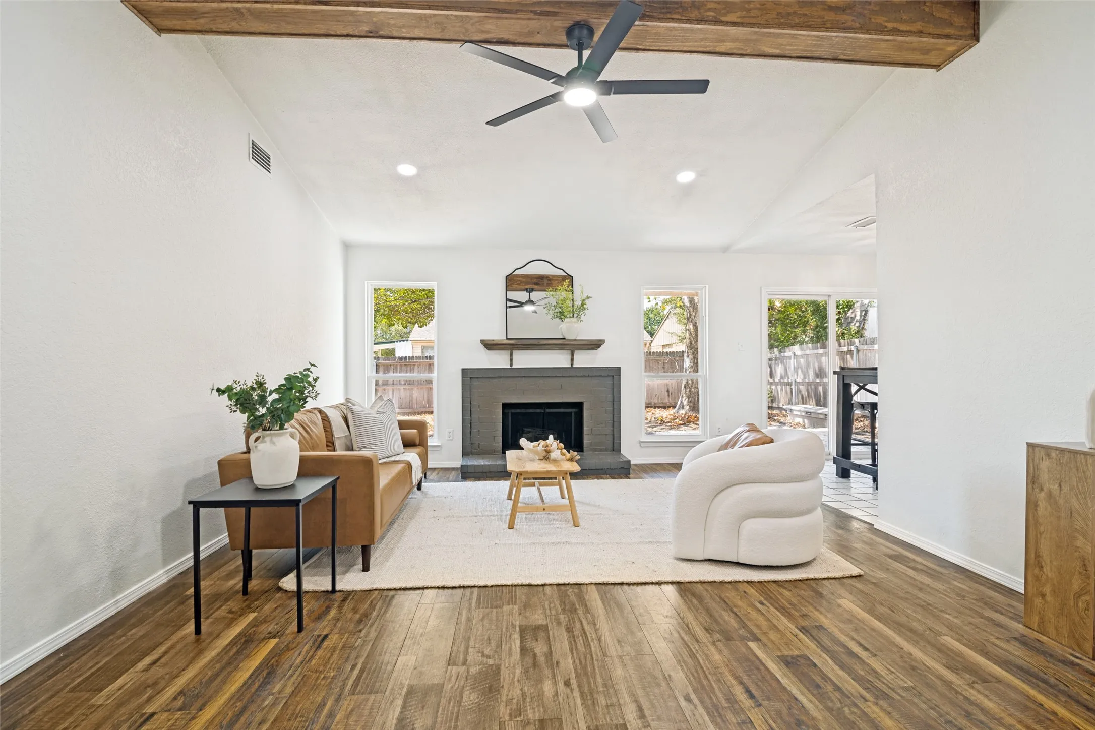 Vaulted ceiling with exposed wood beams, wood-finish flooring, recessed lighting, and a dark stone fireplace with a wood mantle
