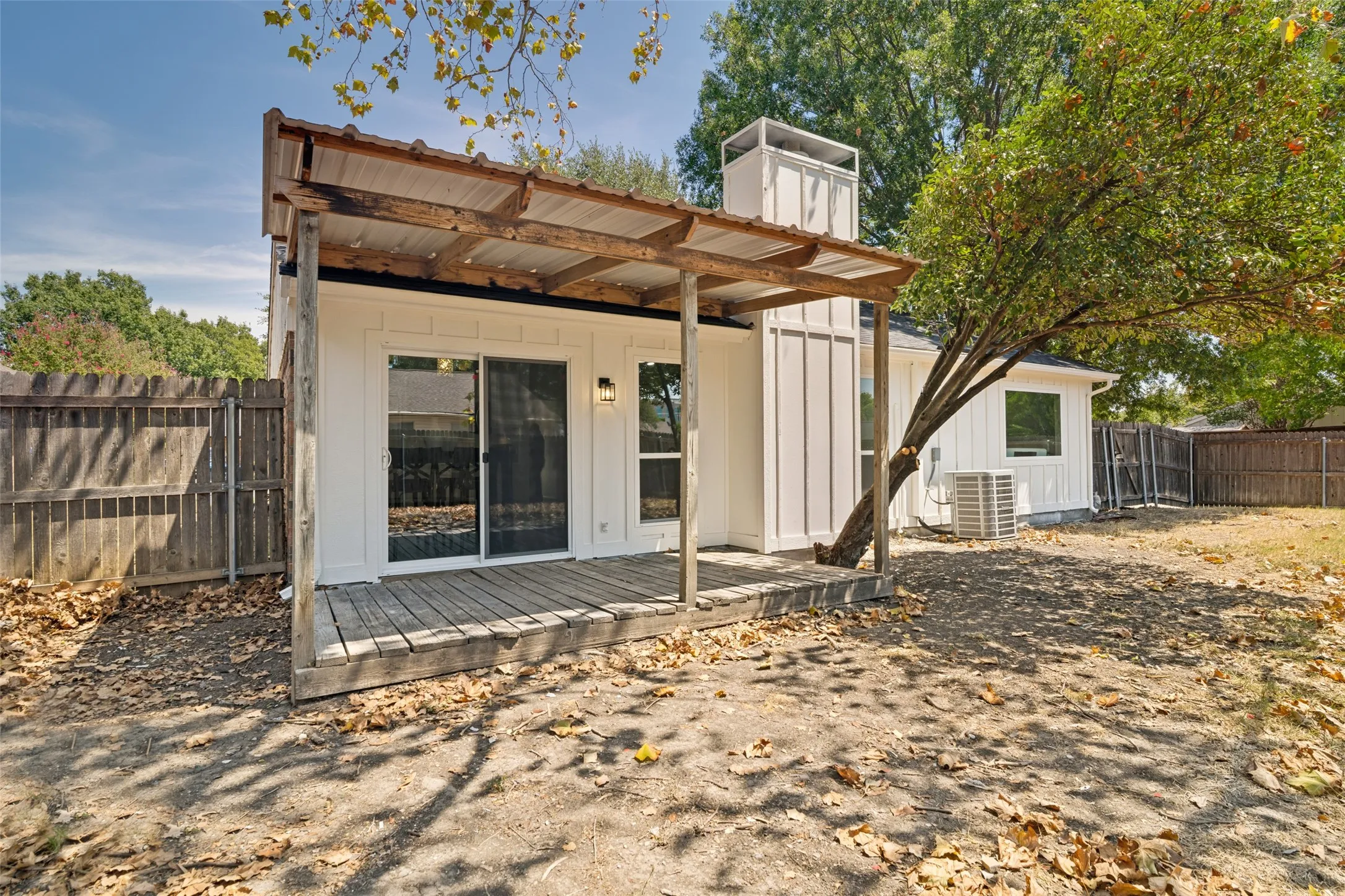 Exterior featuring a wood deck, sliding glassdoor, white vertical siding, and a wooden fence