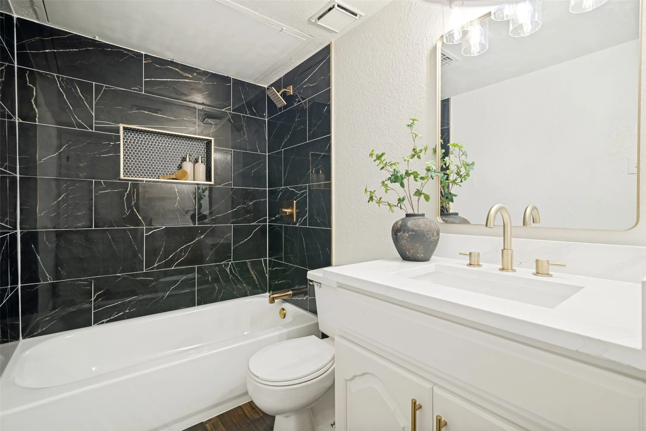 Bathroom featuring a white bathtub, black veined wall tile, built-in shower niche, white vanity with integrated sink, and brass-finish fixtures