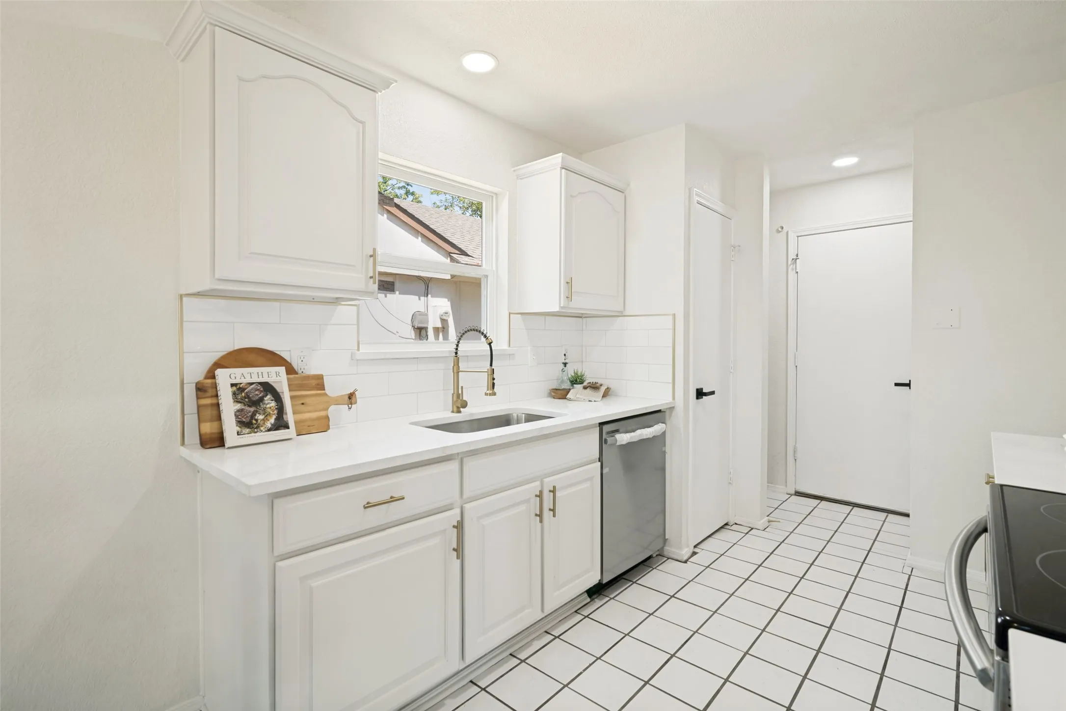 Kitchen featuring white cabinetry, subway tile backsplash, white countertops, stainless steel dishwasher, and square tile flooring