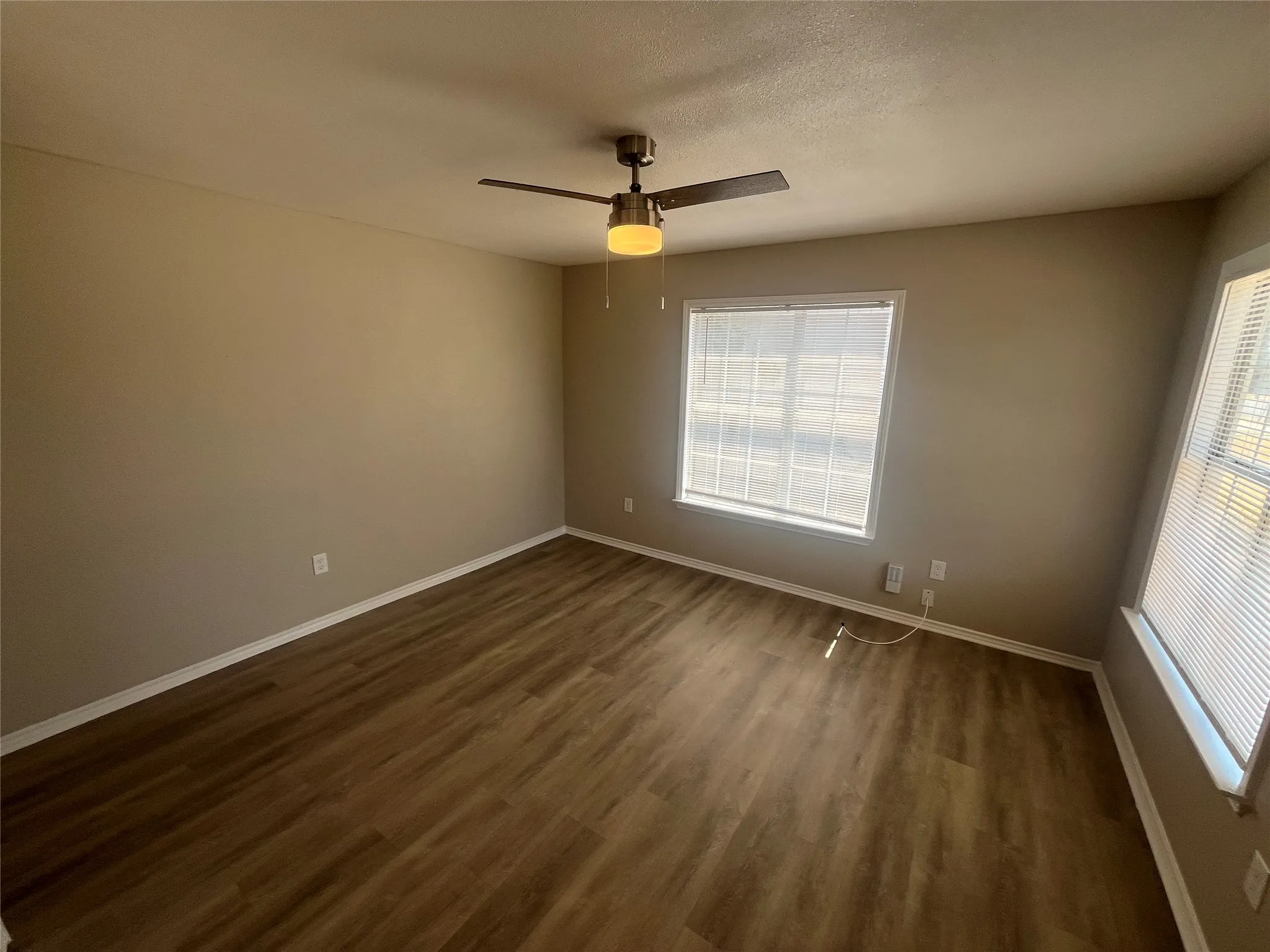 Wood-finish flooring, neutral wall color, ceiling fan, and multiple windows with blinds