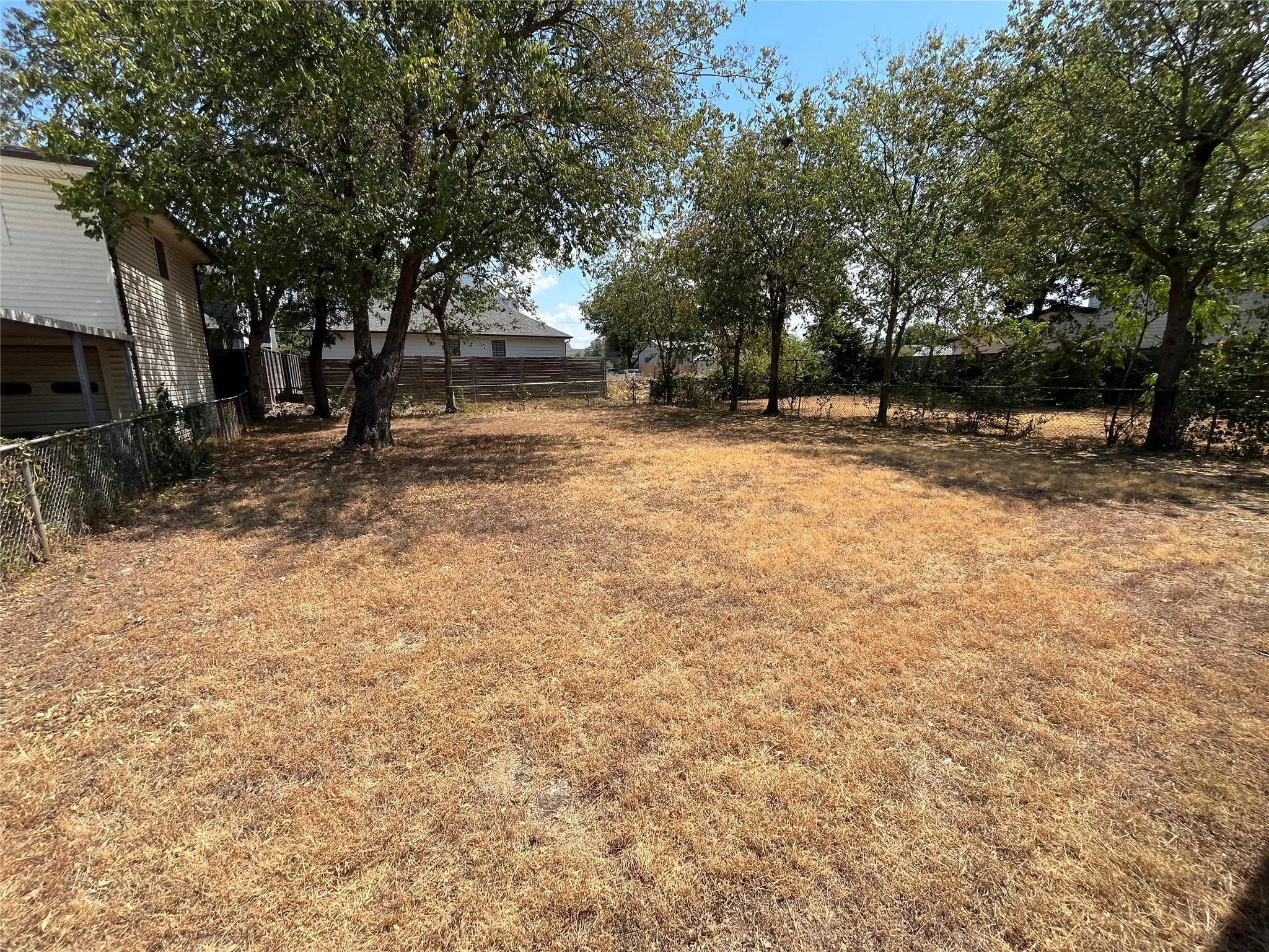 Expansive yard with mature trees providing shade, enclosed by a chain-link fence
