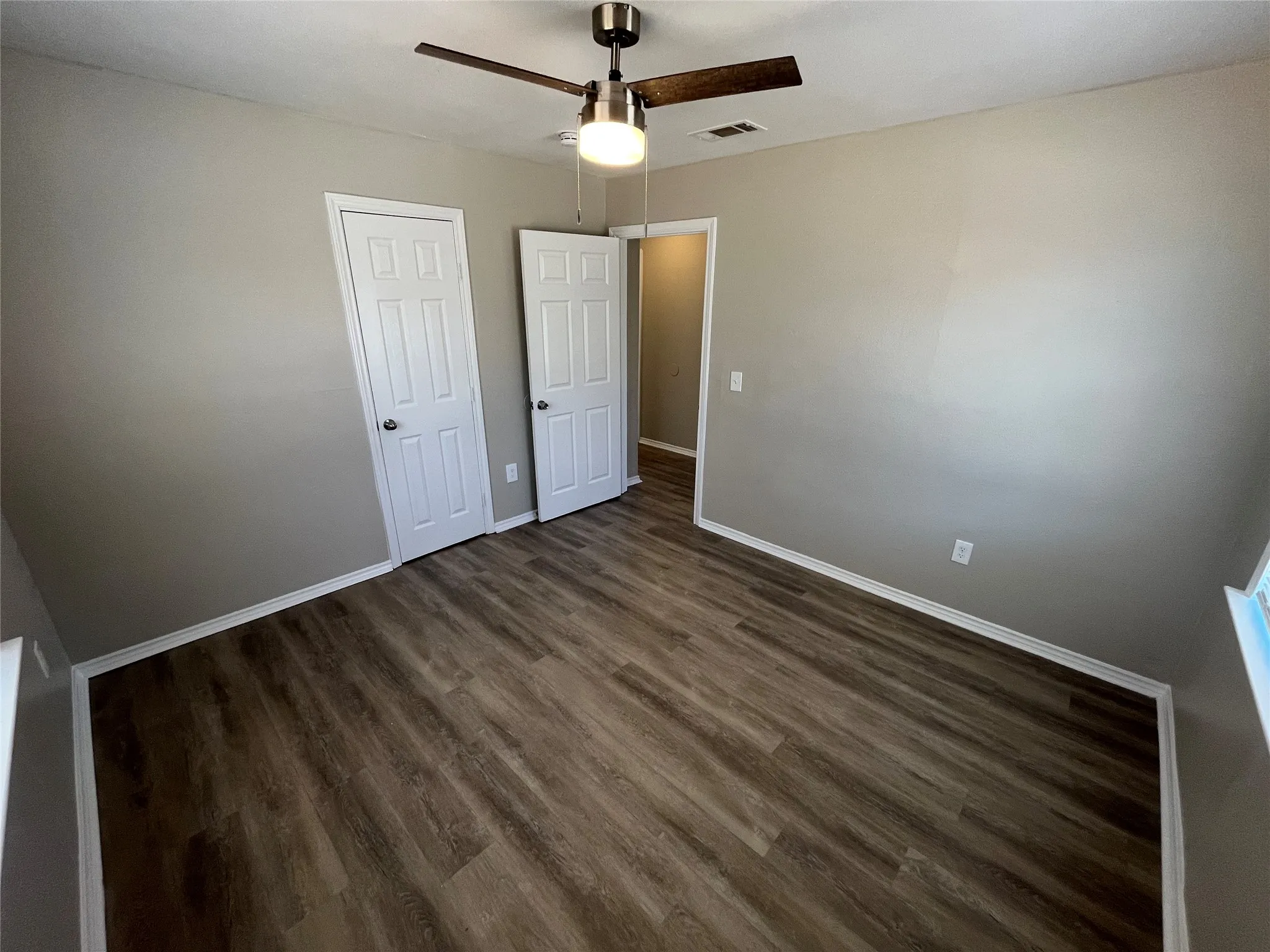 Wood-finish flooring, neutral wall tones, ceiling fan with integrated lighting, and white paneled doors