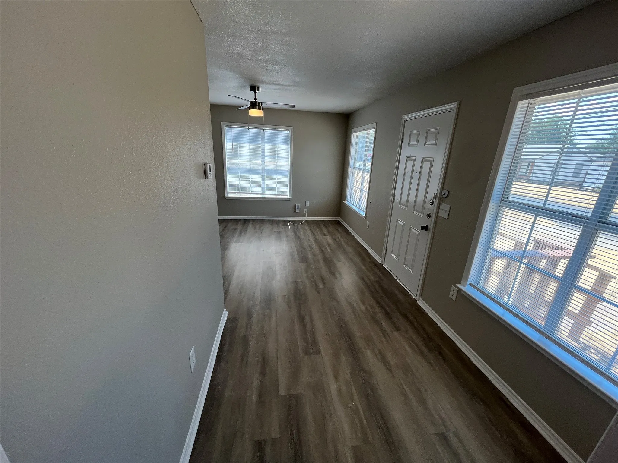 Wood-finish flooring throughout, multiple windows with blinds, ceiling fan with integrated lighting, and a paneled entry door