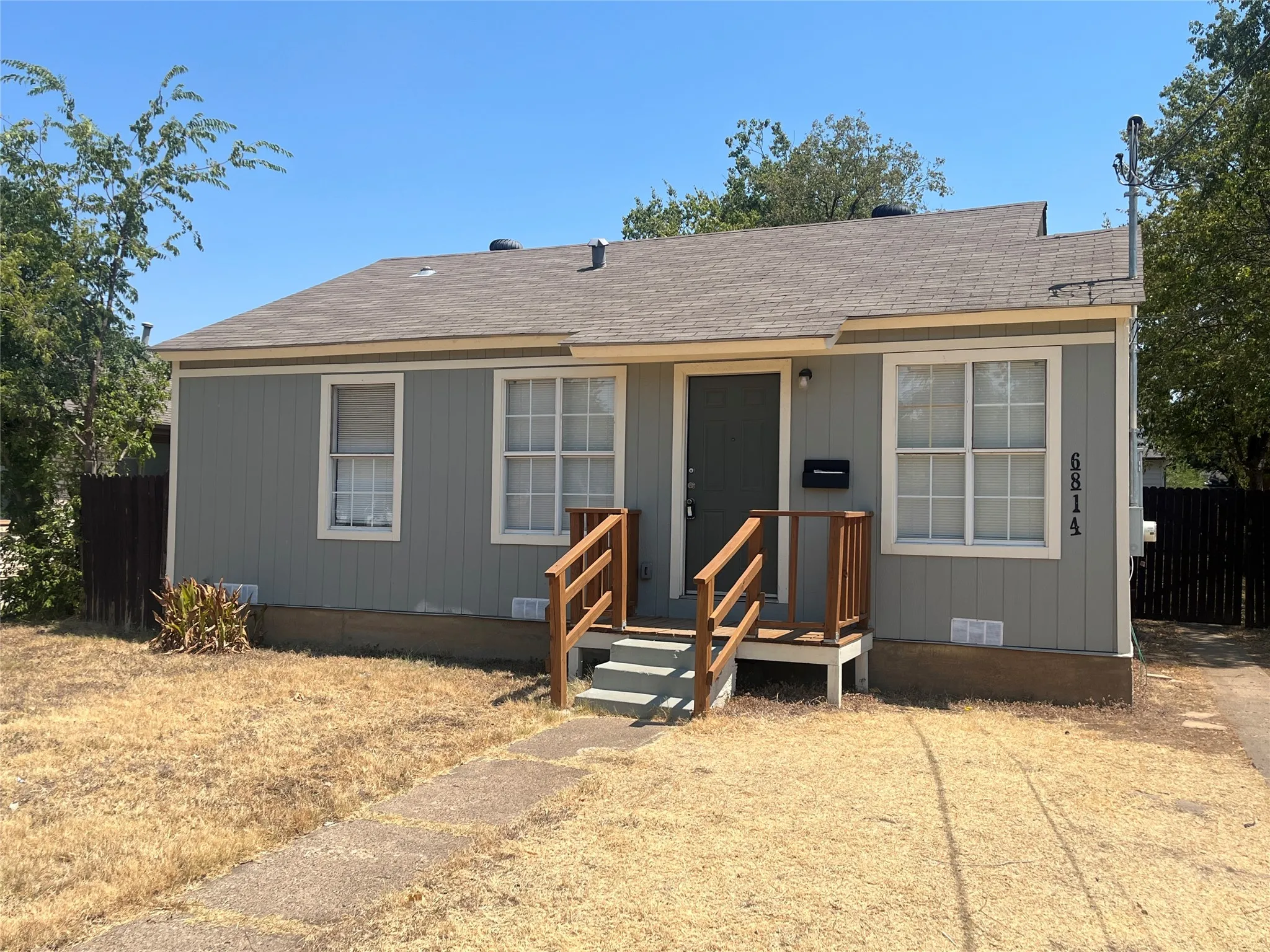 Light gray vertical siding exterior with white window trim, a brown wood-finish front porch railing, and a dark front door
