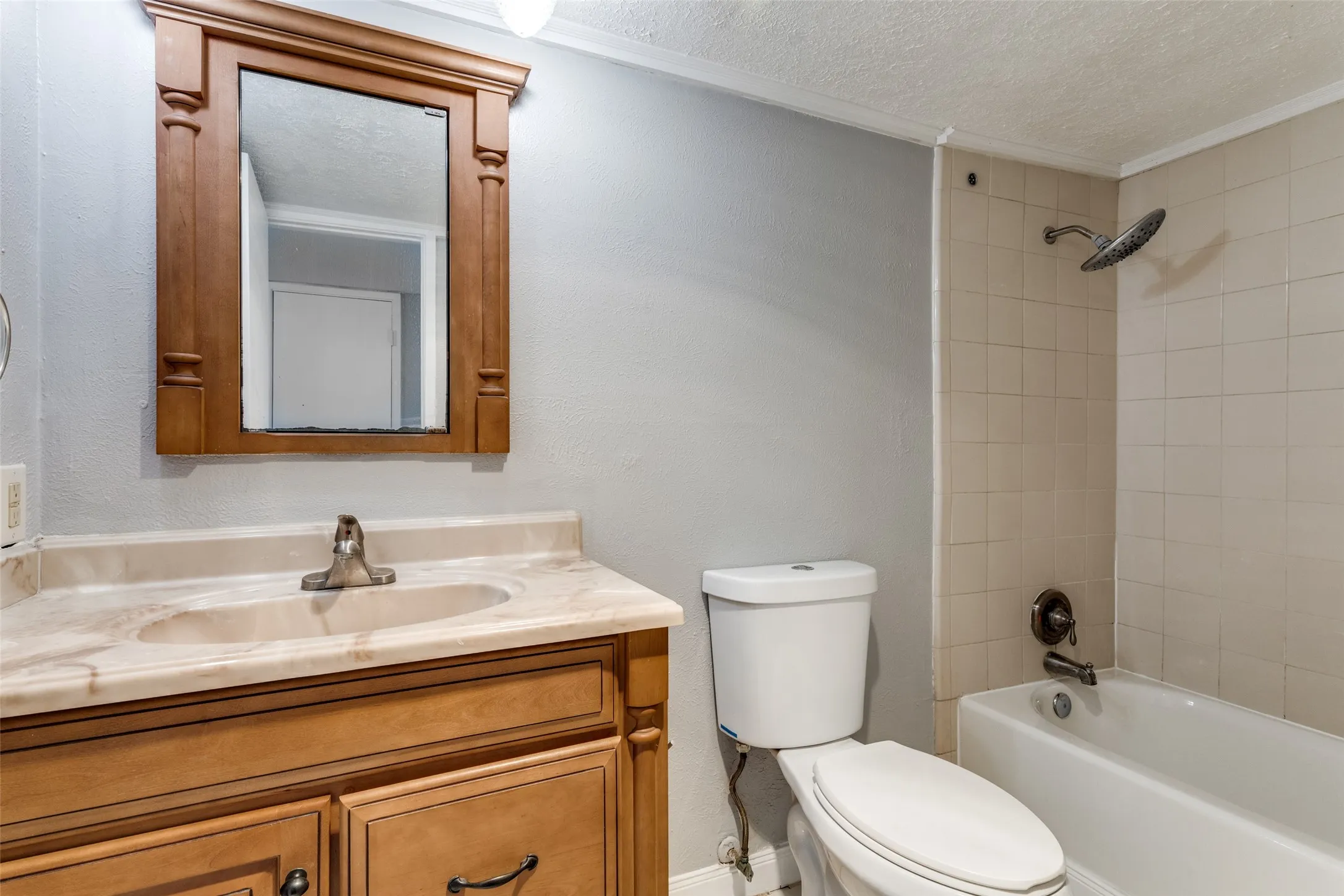 Full bathroom featuring a  wood-tone vanity, cultured marble countertop, single basin sink, framed mirror and a tiled tub/shower combination