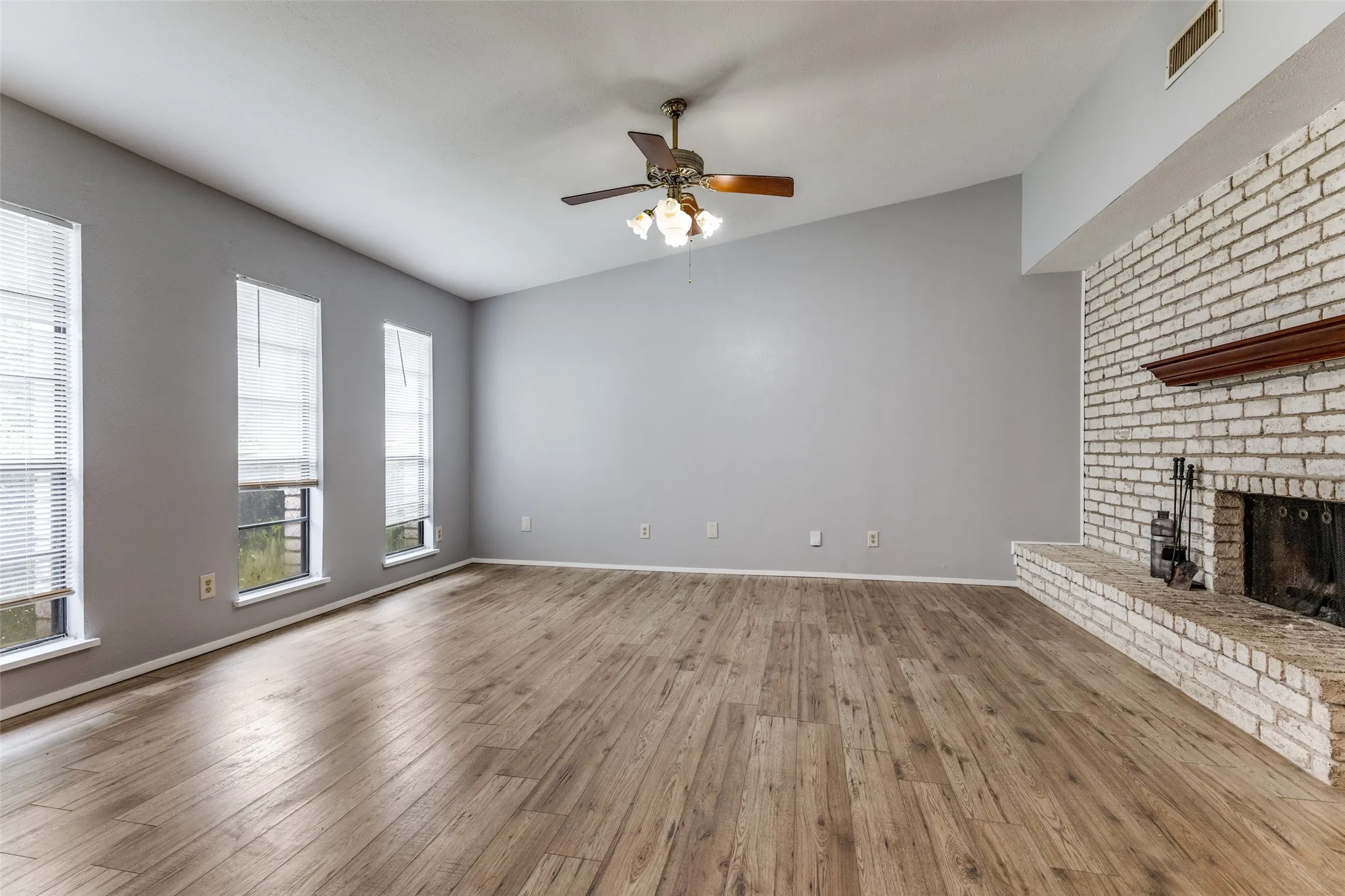 Vaulted ceiling, wood-finish flooring, white brick fireplace, wood mantel, and multiple windows