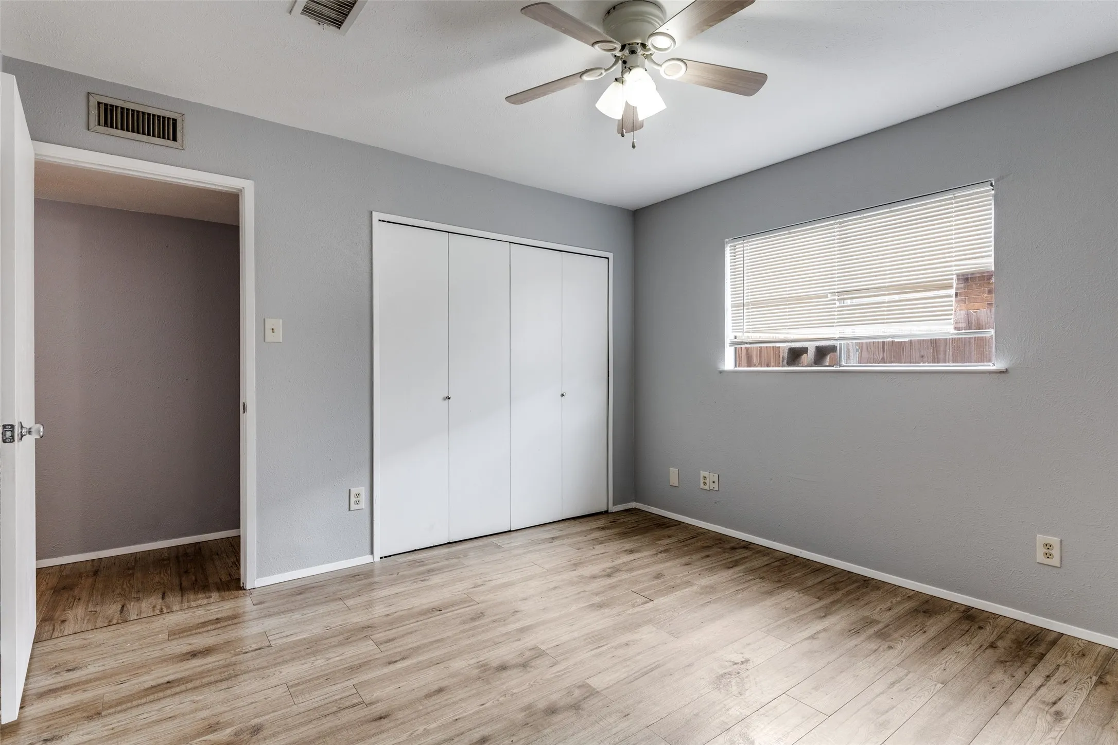 Wood-finish flooring with light gray wall paint, closet, large window with blinds, and a ceiling fan