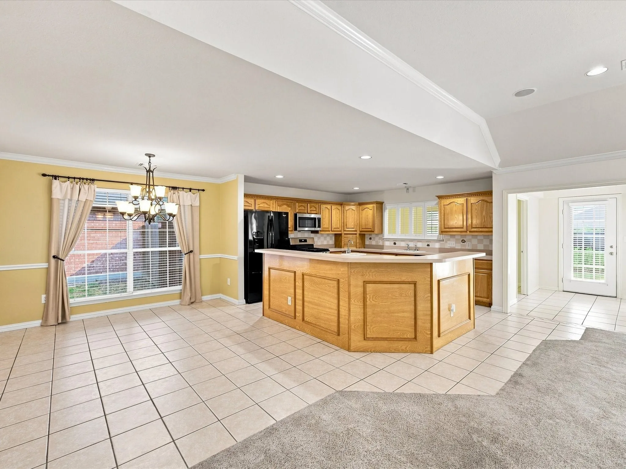 Spacious kitchen featuring light-toned cabinetry, integrated black appliances, and a central island with countertop seating