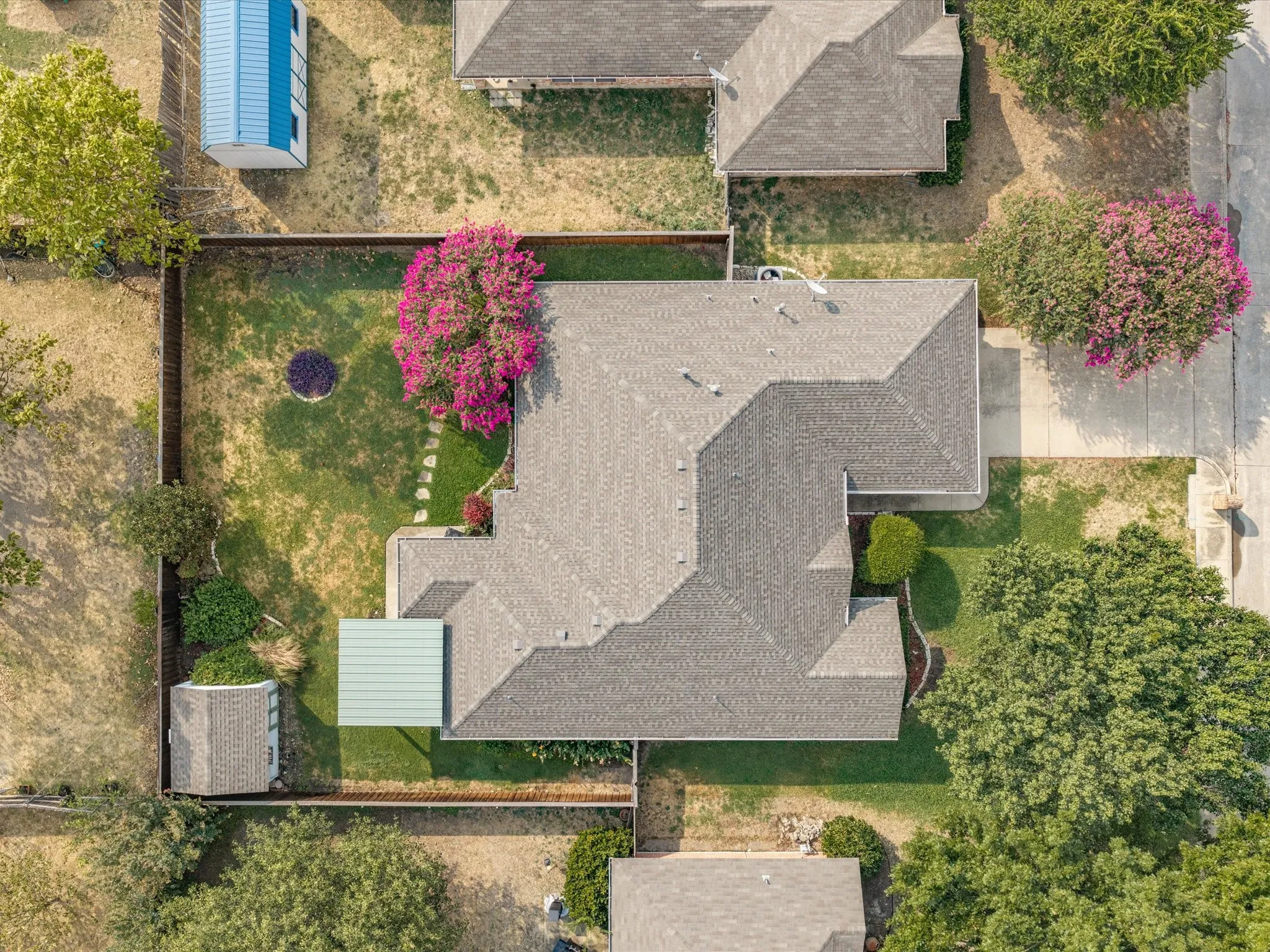 Asphalt shingle roof, paved patio, mature trees, landscaped shrubbery, and stone pathway