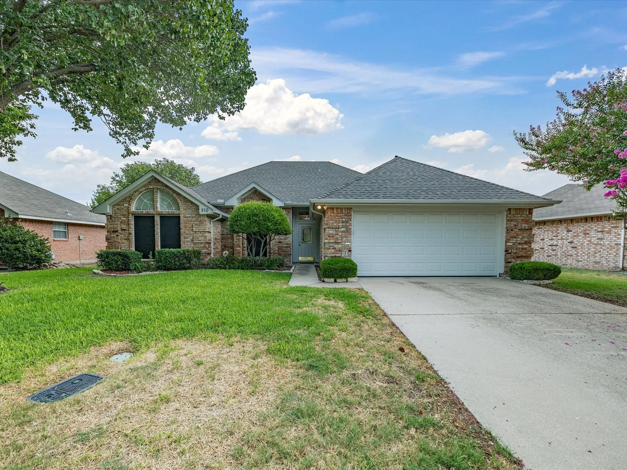 Brick and stone exterior with an attached garage, featuring a concrete driveway and mature trees