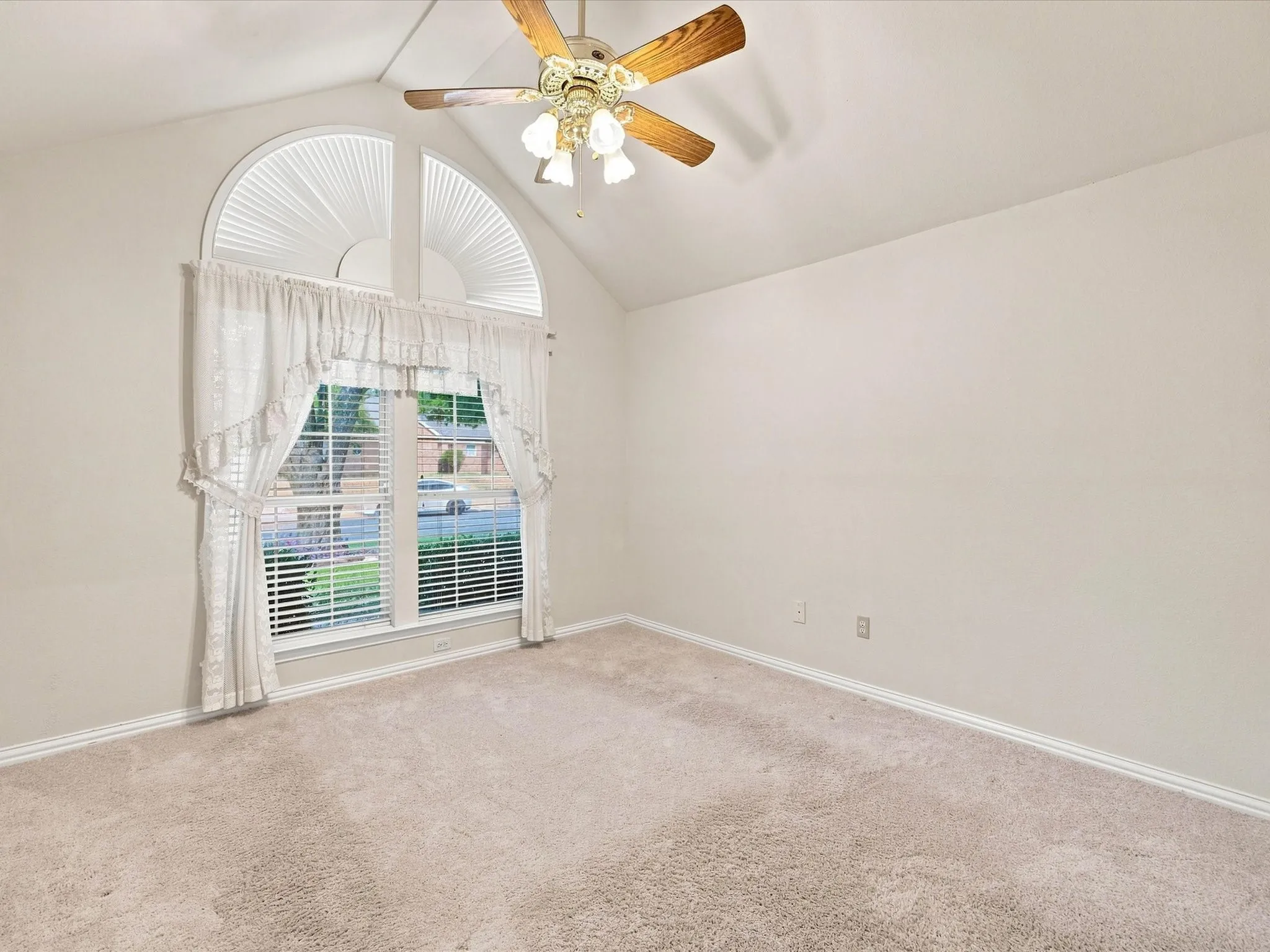 Vaulted ceiling, arched window with blinds, ceiling fan with integrated lighting, and carpeted flooring