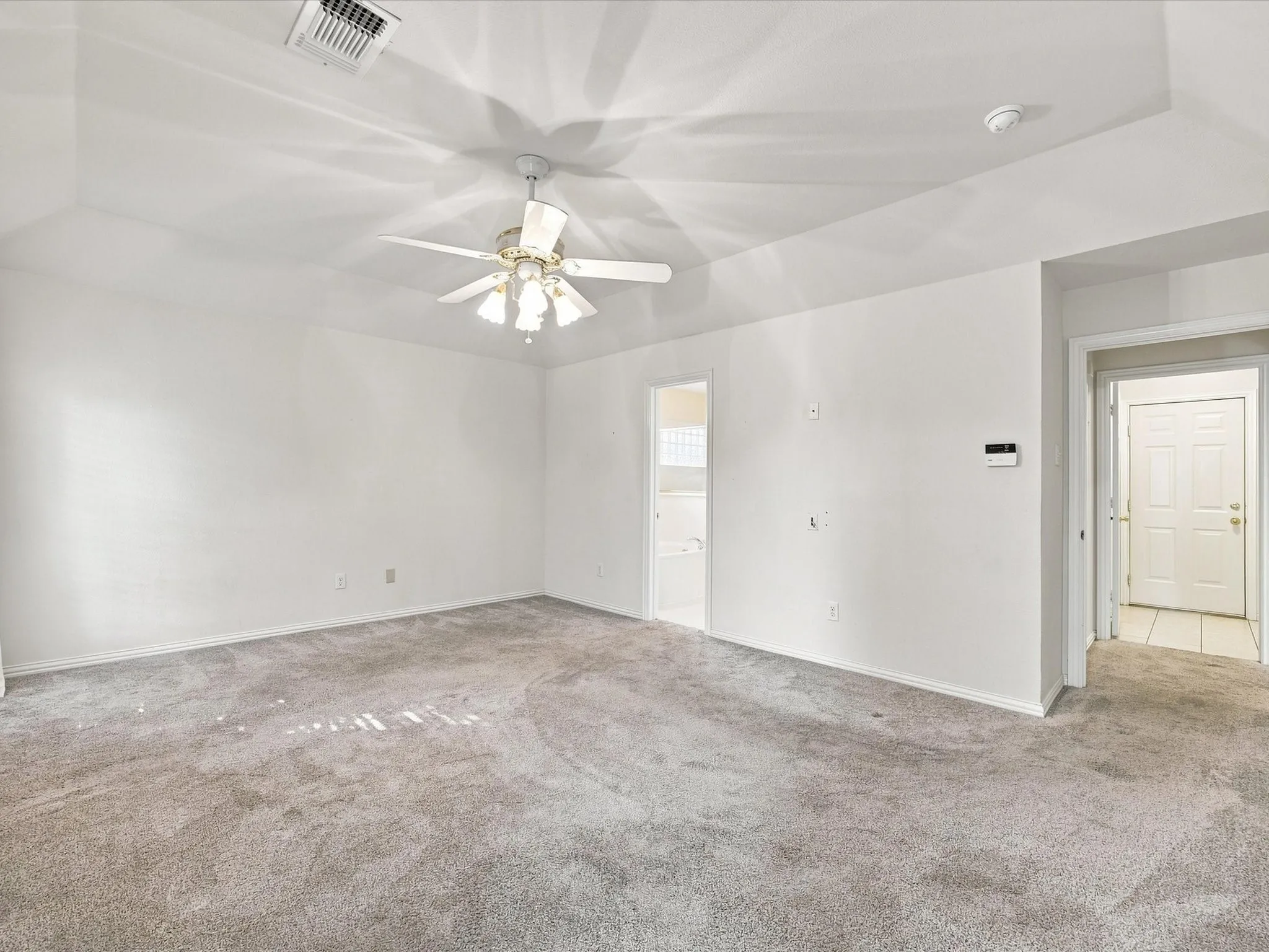Spacious interior room with light gray carpet, white walls, and a ceiling fan with integrated lighting