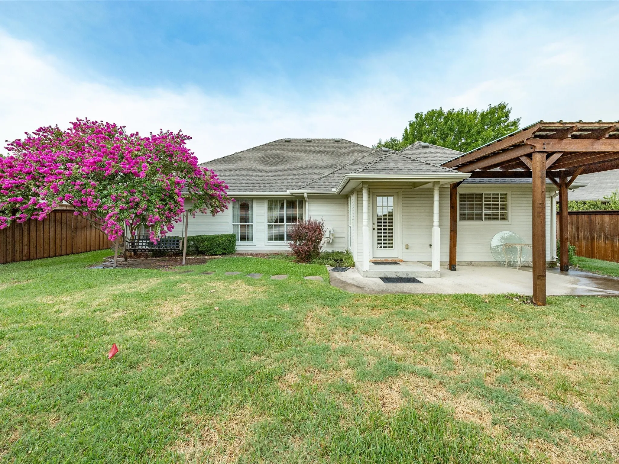 Expansive backyard featuring a manicured lawn, established flowering tree, wood privacy fencing, concrete patio, and a wood pergola