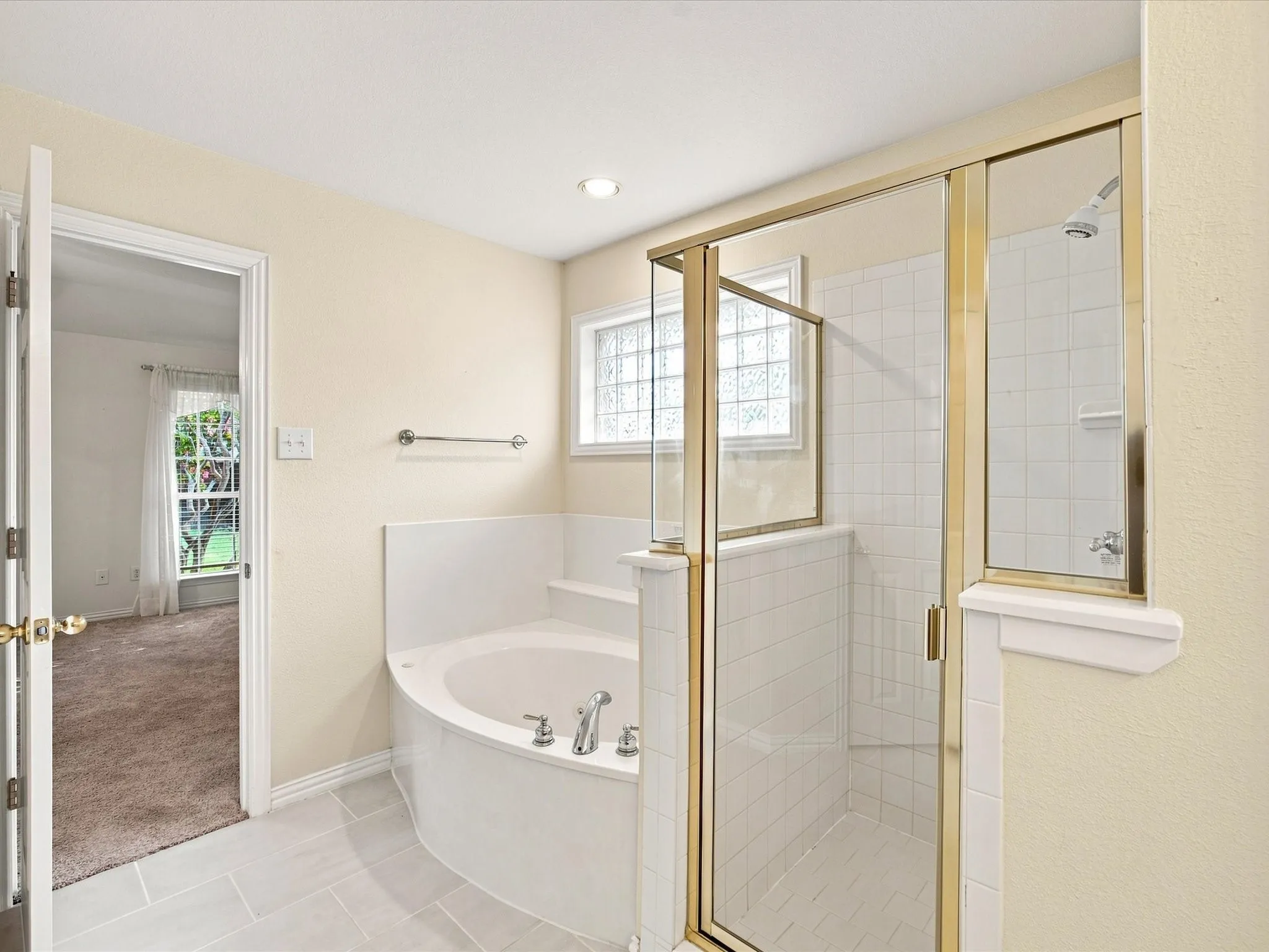 Built-in corner soaking tub with chrome fixtures, glass-enclosed shower with white tile surround, and light-toned floor tile