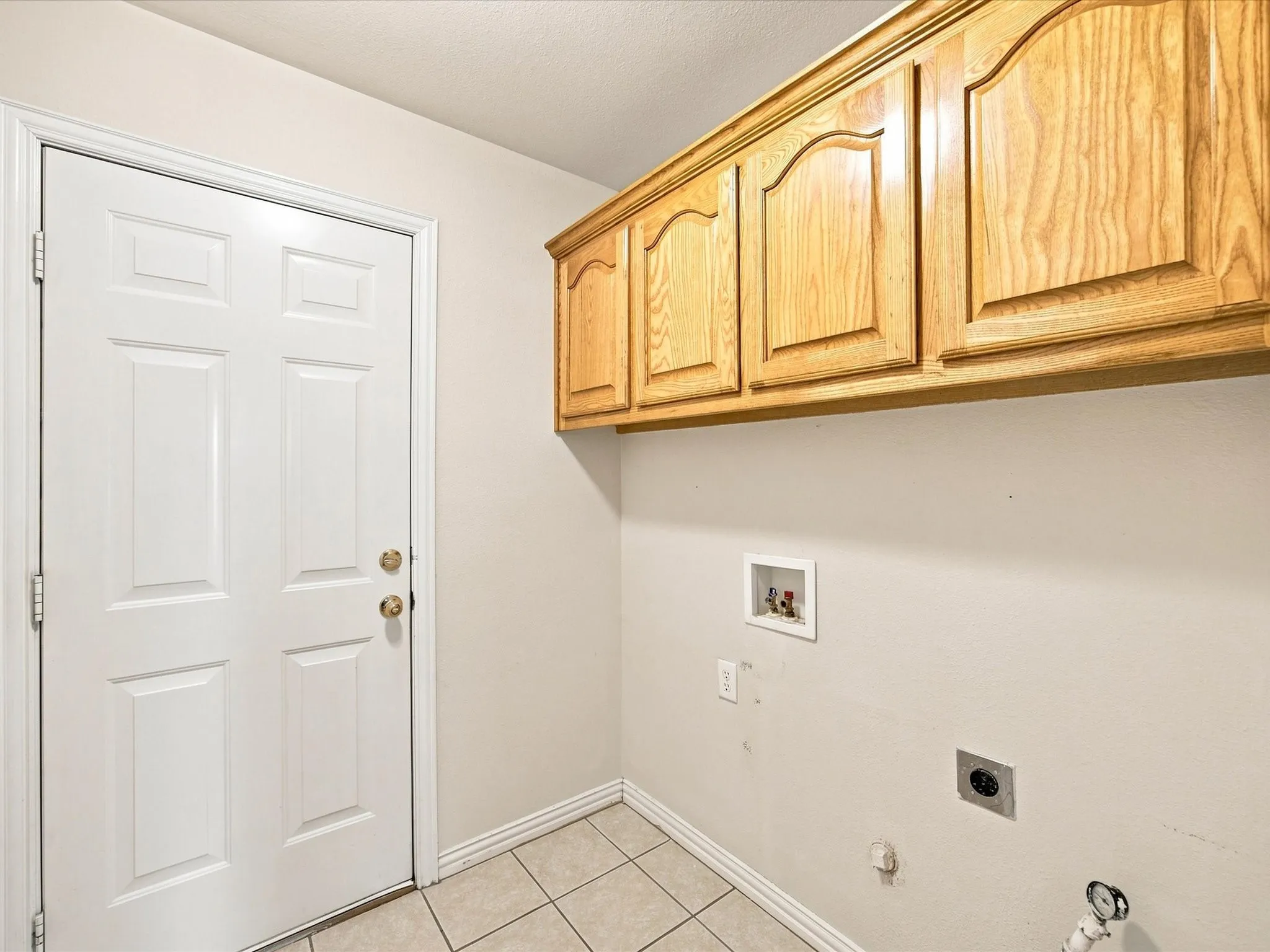 Wood-finish upper cabinetry, tiled flooring, white paneled door, and appliance connections