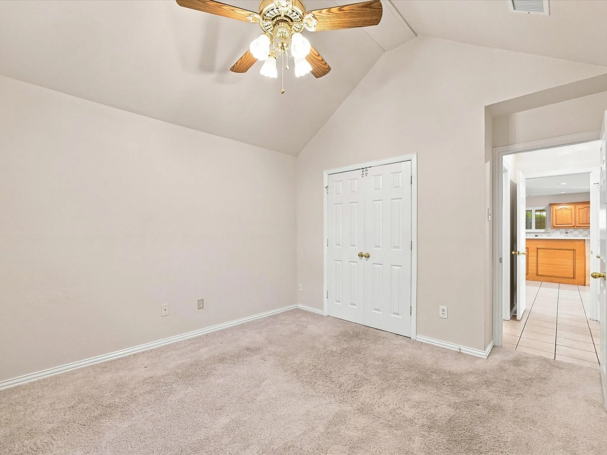 Vaulted ceiling with a wood-finish ceiling fan, neutral wall paint, and white trim