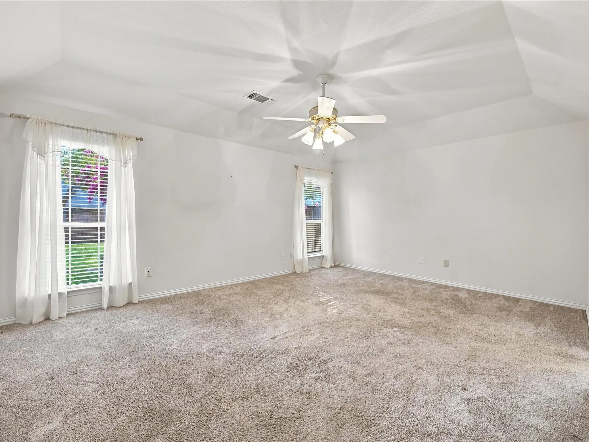 Tray ceiling with a ceiling fan light fixture, two windows, and light-colored carpeting