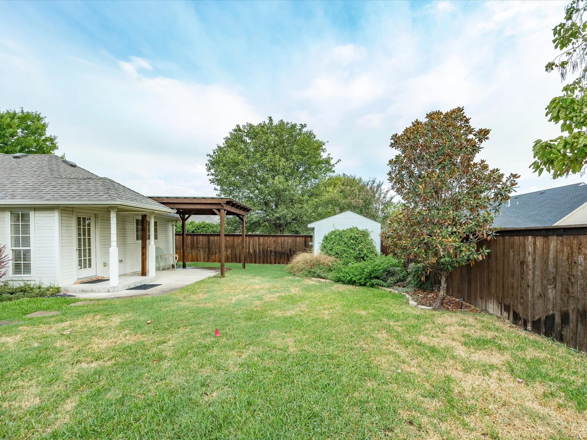 Expansive backyard featuring a concrete patio, a wooden pergola, a storage shed, and mature trees