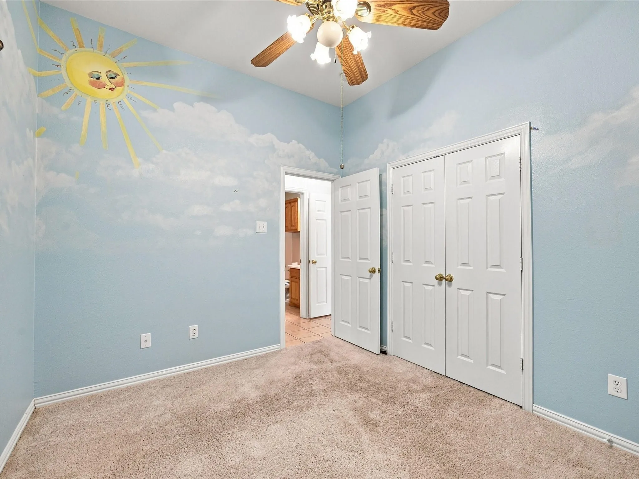 Carpeted room featuring a ceiling fan with light fixture, built-in bi-fold closet doors, and painted wall murals