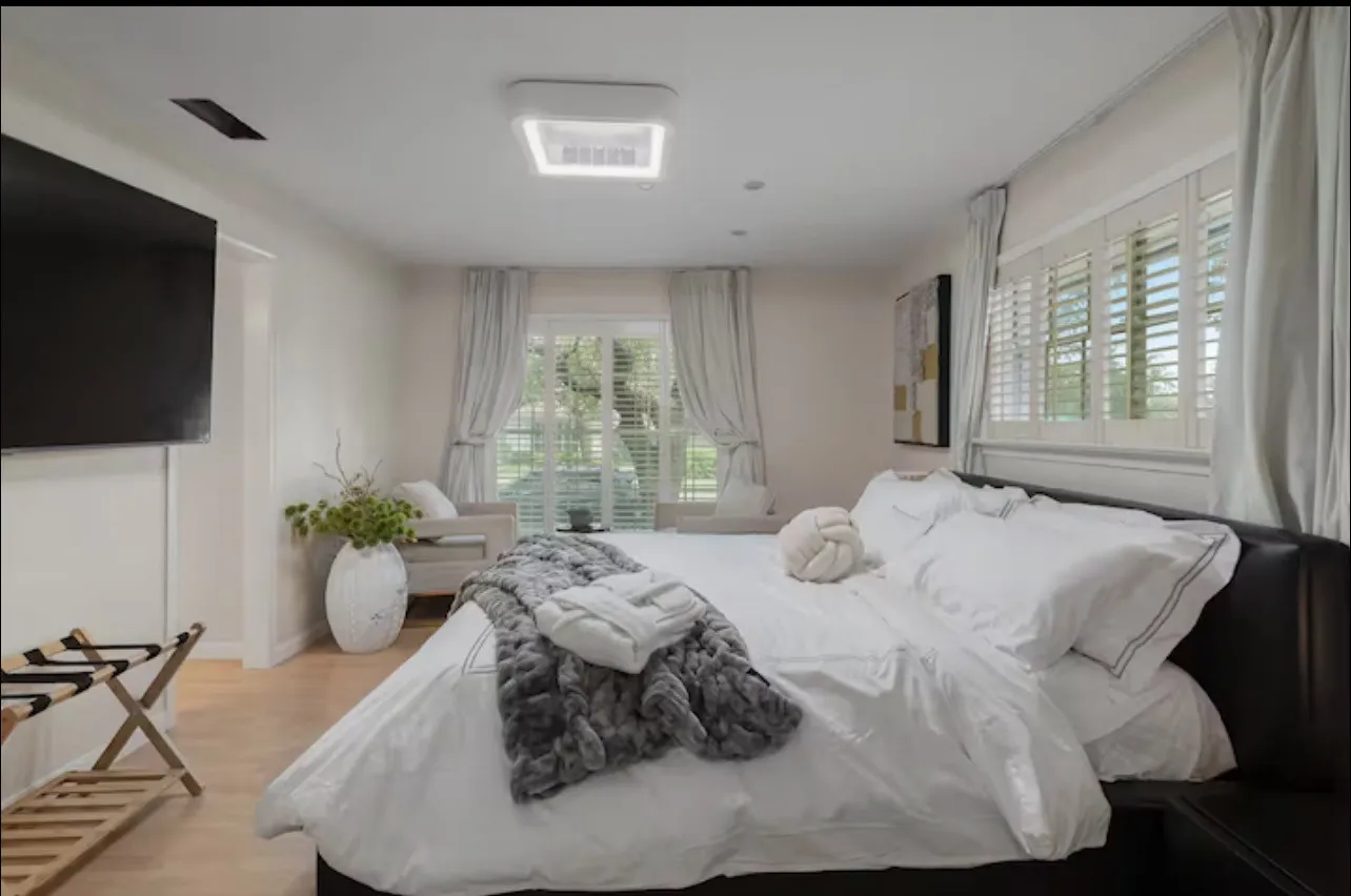Recessed ceiling light, light wood-finish flooring, white plantation shutters, built-in window seating, and a mounted flat-screen television