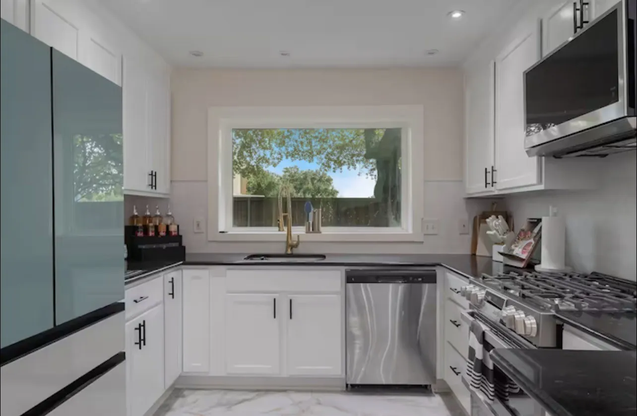 White shaker cabinetry with black hardware, dark countertops, a stainless steel dishwasher, a gas range, and marble-look flooring