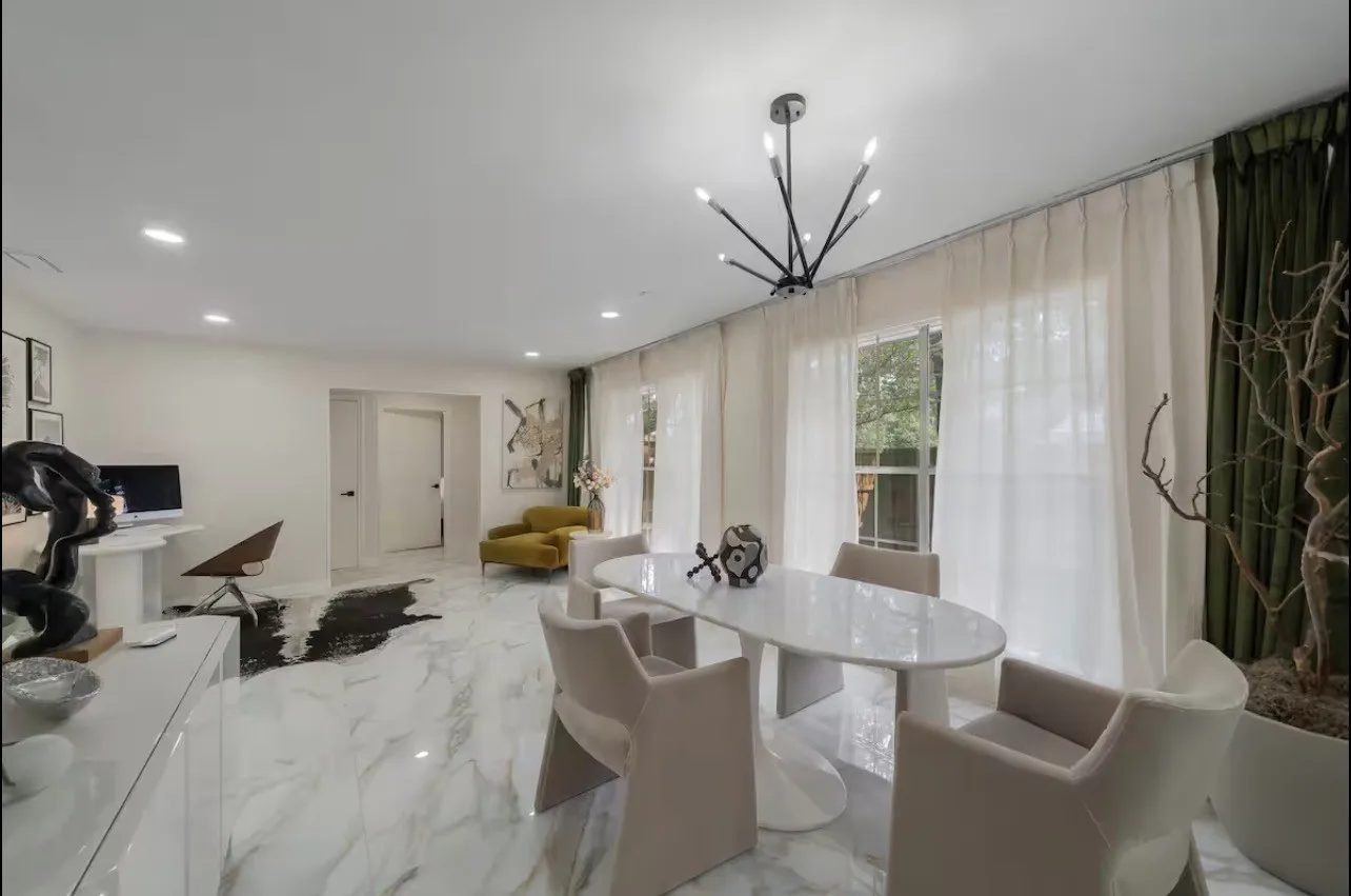 Recessed lighting, large windows, white marble-look flooring, and a modern black chandelier