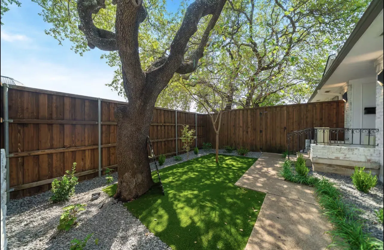 Private outdoor area featuring a mature tree, wood privacy fencing, artificial turf, and a concrete pathway