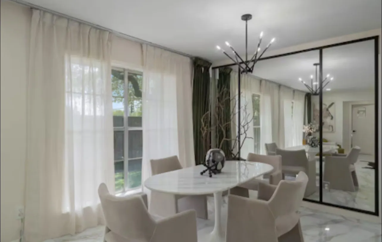 Wall-mounted full-length mirrors with dark frames, a modern chandelier, and large windows with sheer white drapery