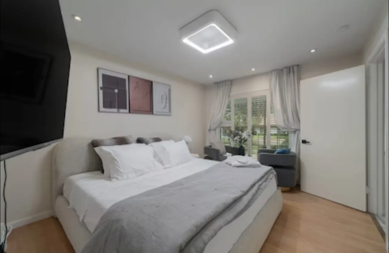 Recessed ceiling lighting, a contemporary square flush-mount fixture, wood-finish flooring, a window with plantation shutters, and a paneled interior door