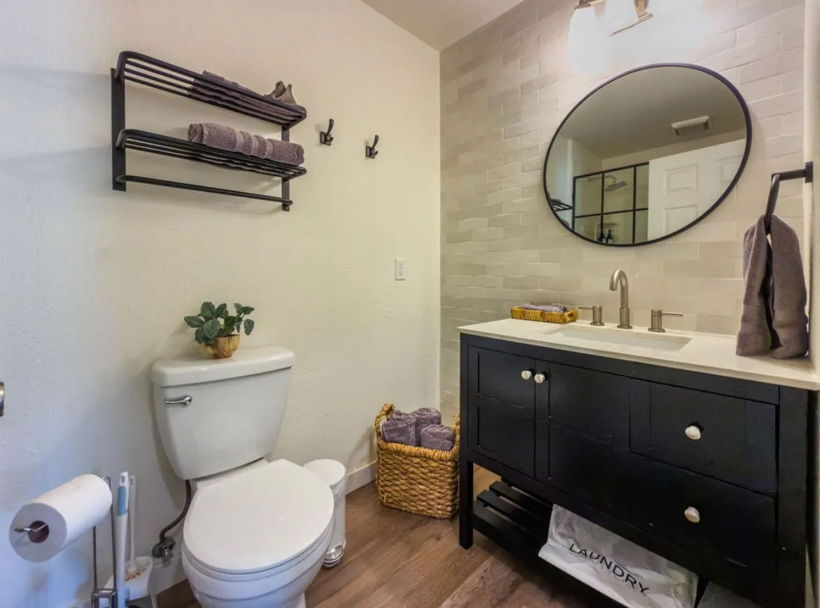 Single vanity with a light countertop, wood-finish flooring, white subway tile wall, and a large oval mirror