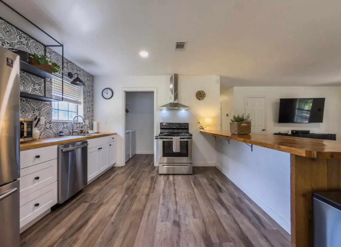 Open-concept kitchen featuring wood-finish flooring, white cabinetry with dark hardware, stainless steel appliances, and a wood-finish countertop