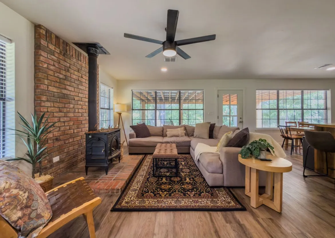 Exposed brick accent wall with a cast iron wood-burning stove, wood-finish flooring, and multiple large windows
